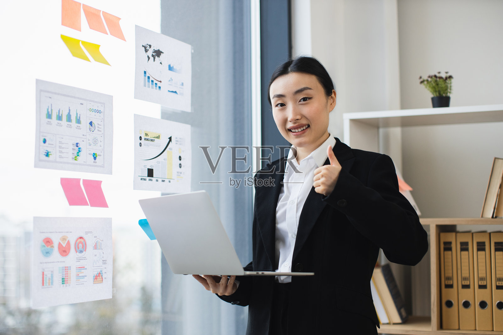 自信的女商人在办公室里举起大拇指，手里拿着笔记本电脑照片摄影图片