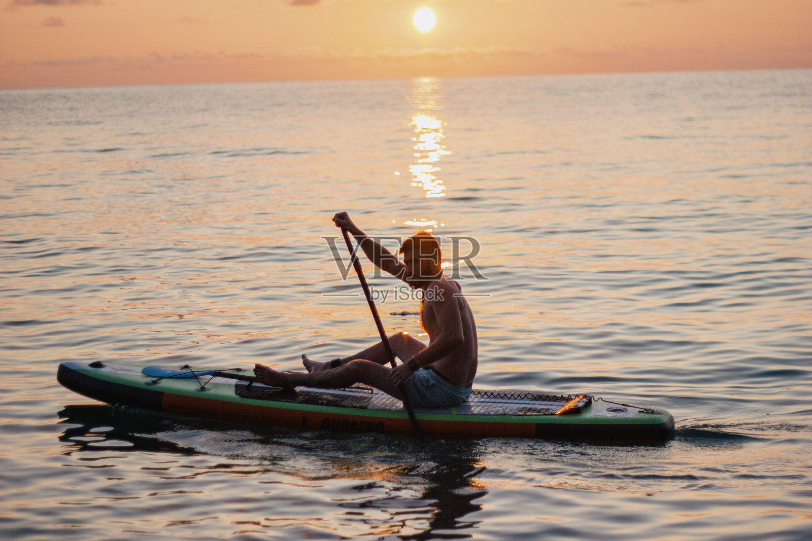 一名男子在海上日落时划着立式划水板。高质量照片照片摄影图片