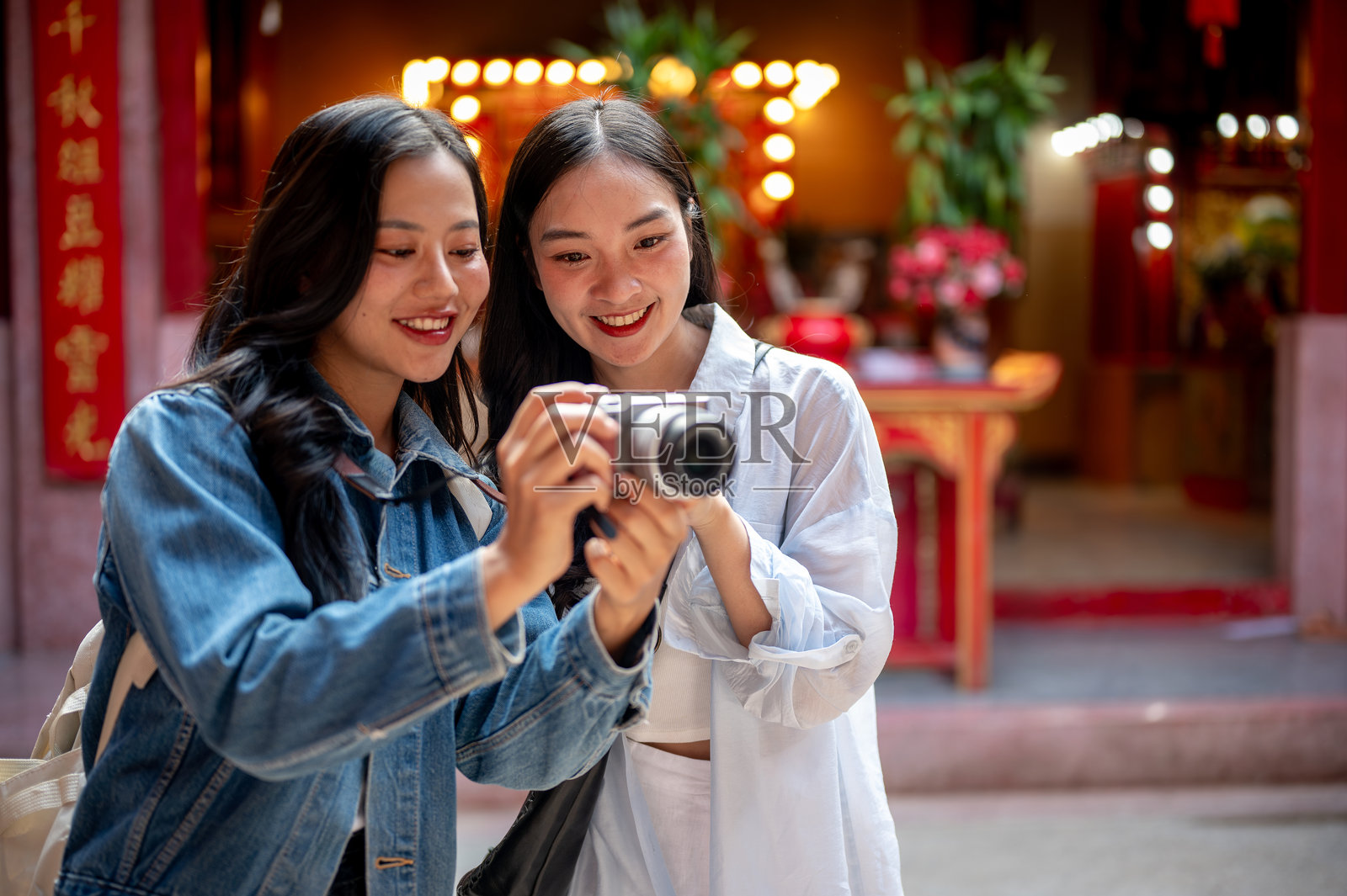两个快乐、美丽的亚洲女性朋友在中国神社参观，一起查看相机里的照片。照片摄影图片