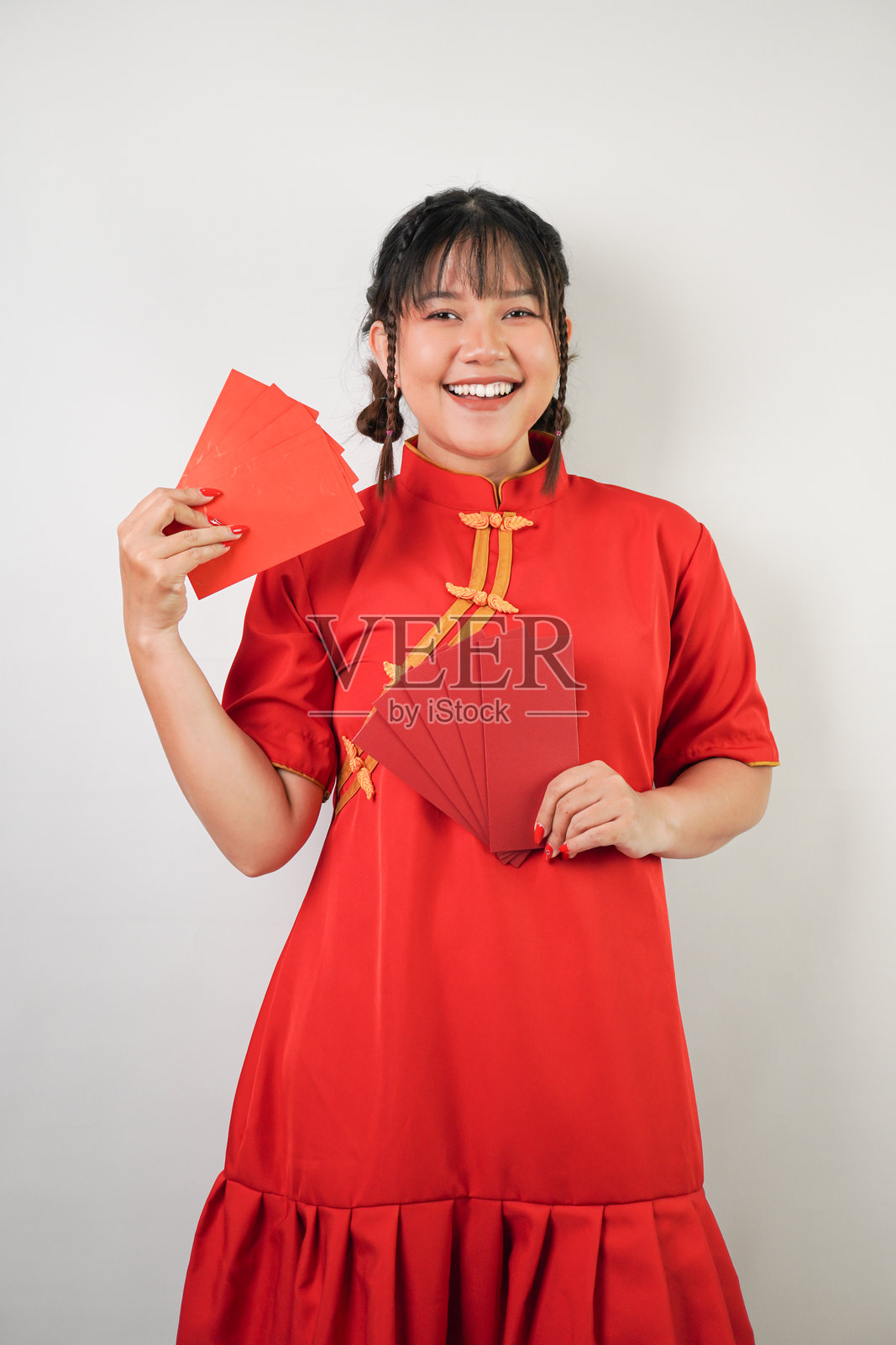 微笑的年轻亚洲女性穿着红色传统中国服装，手里拿着许多红包，背景为白色。适合春节派对的概念。照片摄影图片