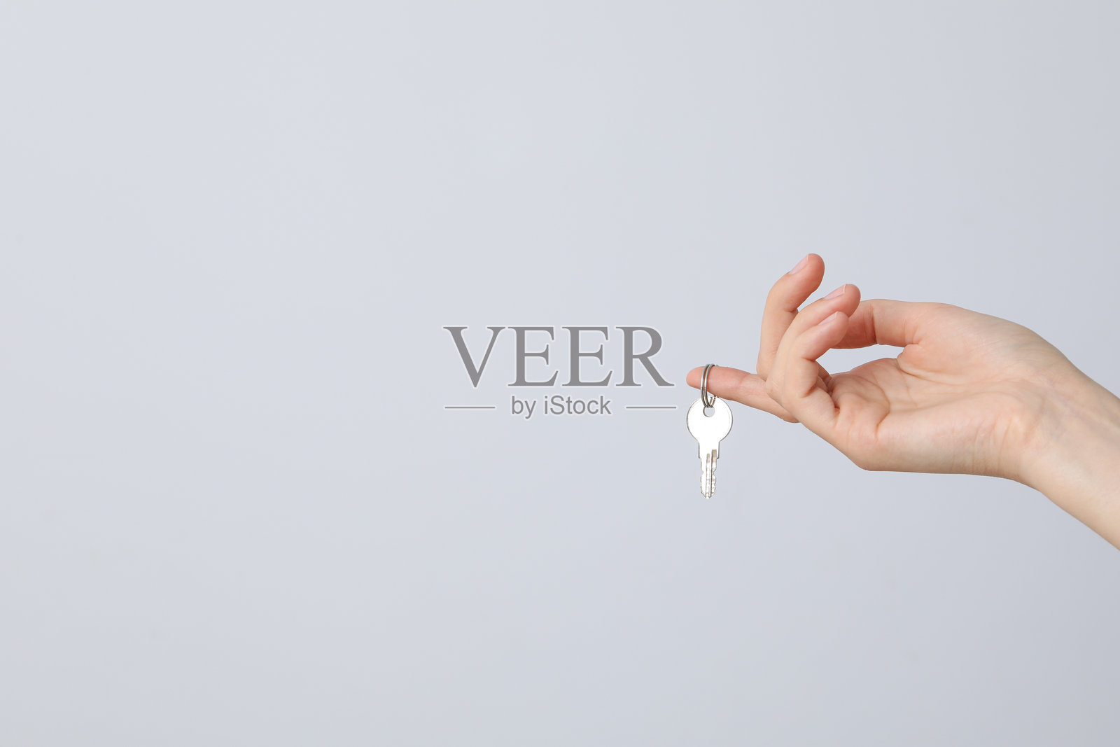 女性手指上戴着钥匙，背景为浅色，留有文字空间照片摄影图片