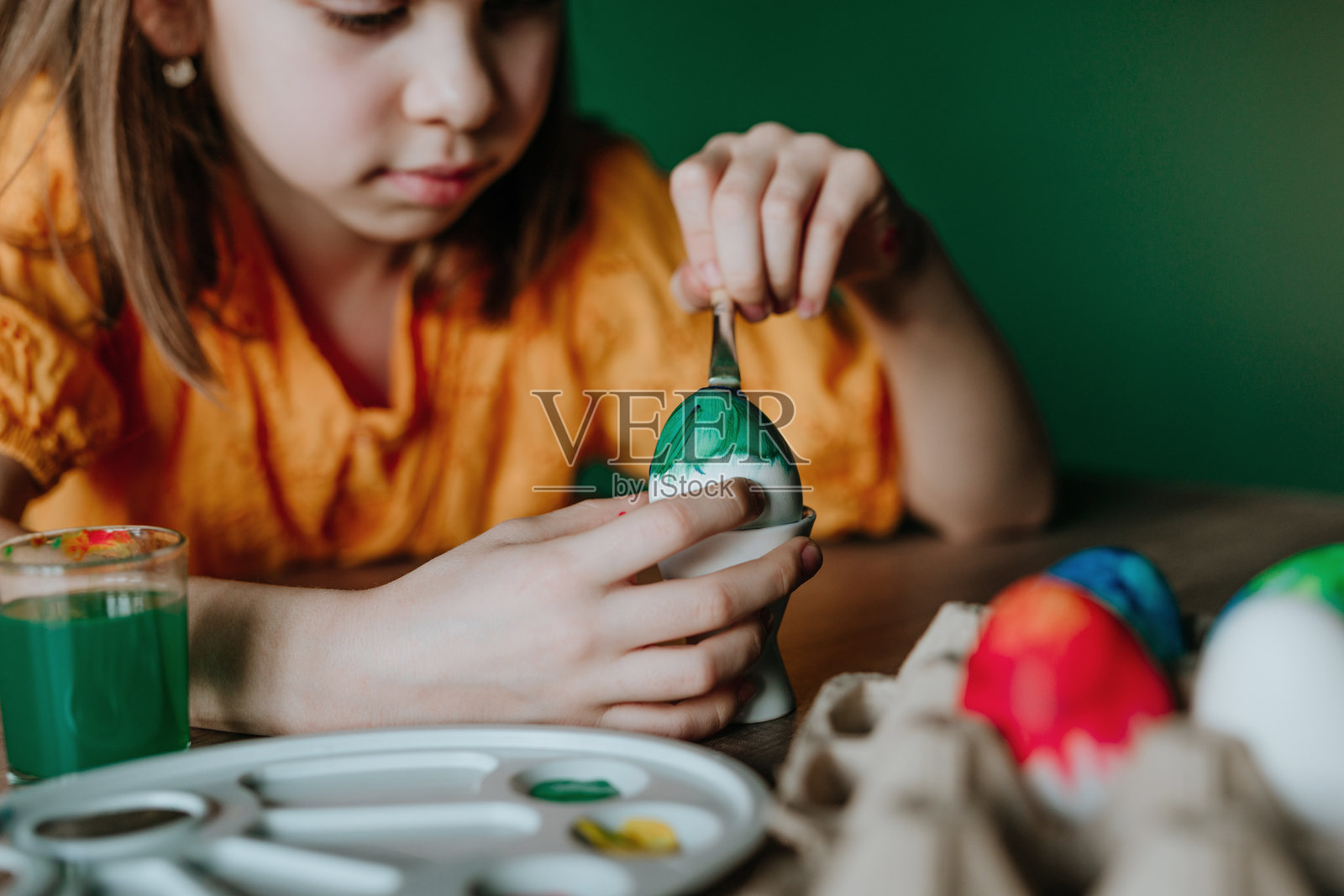 小女孩在绿色墙壁前的桌子上专心绘制彩蛋的特写镜头照片摄影图片