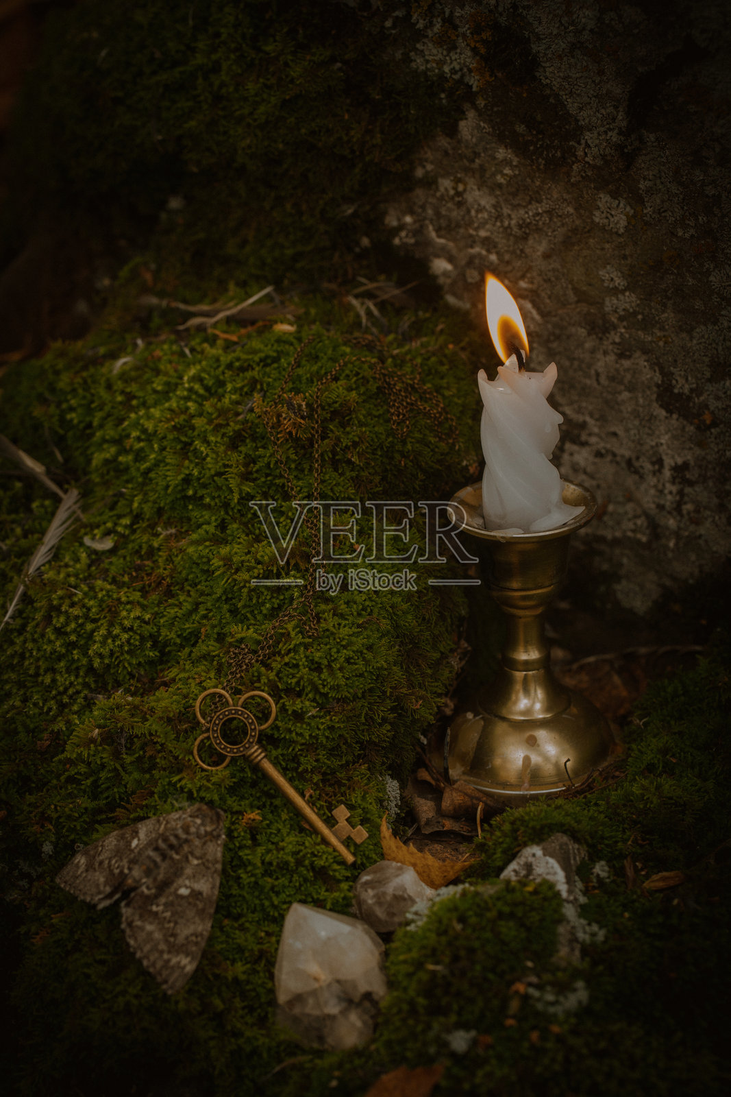 绿色苔藓上的燃烧蜡烛、青铜钥匙和一只死蛾，森林中，特写，竖版，选择性对焦。照片摄影图片