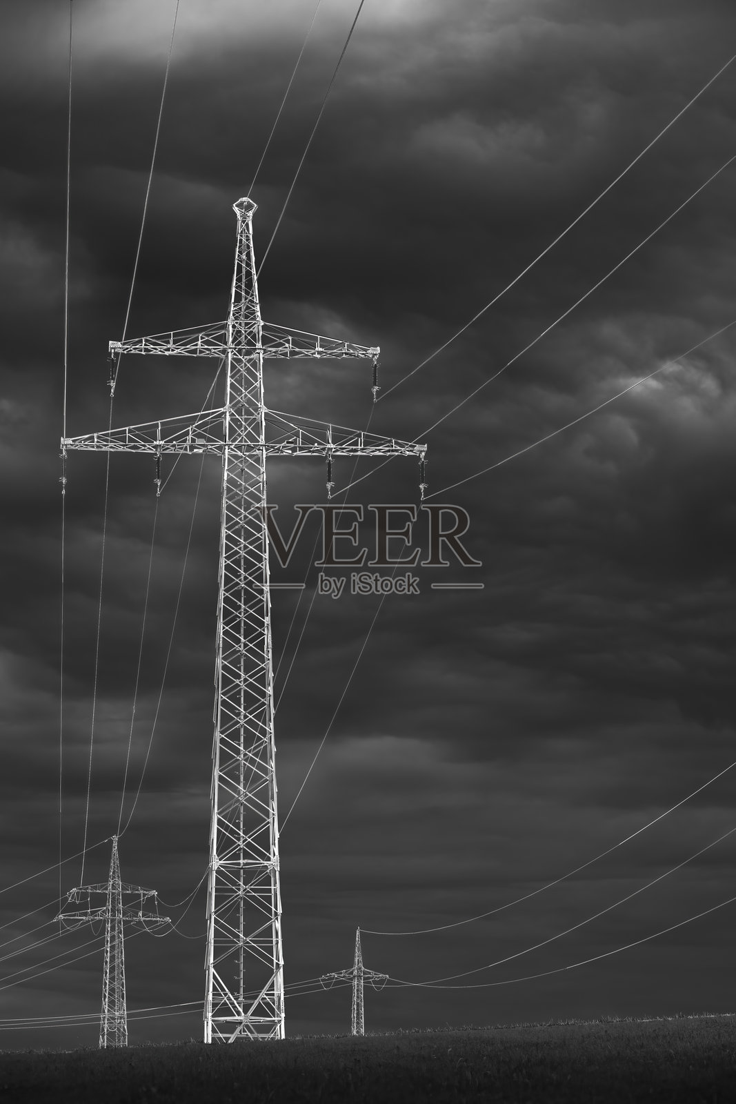 黑白色调下，戏剧性天空中的高压电塔与电缆照片摄影图片