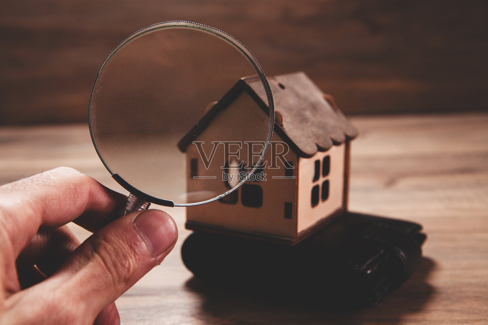 放大镜与木桌上的微型房屋。房地产和物业概念照片摄影图片