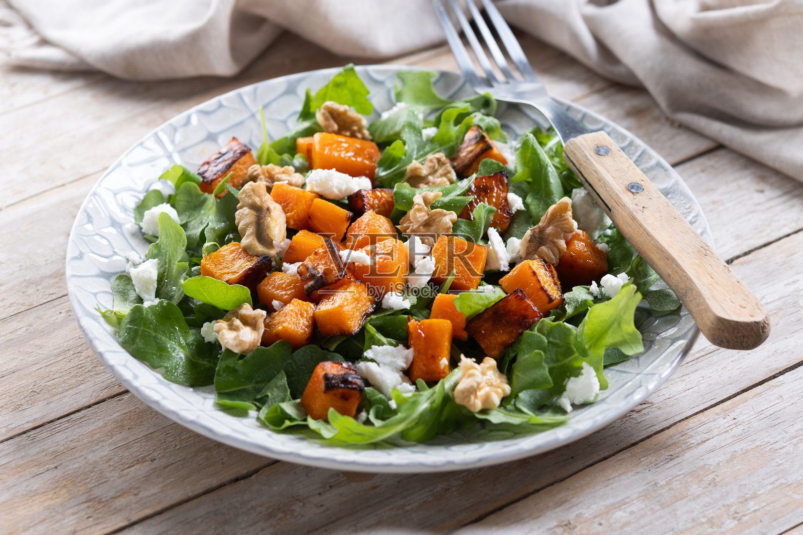 木质餐盘上的南瓜沙拉，配有芝麻菜、核桃和羊奶酪照片摄影图片