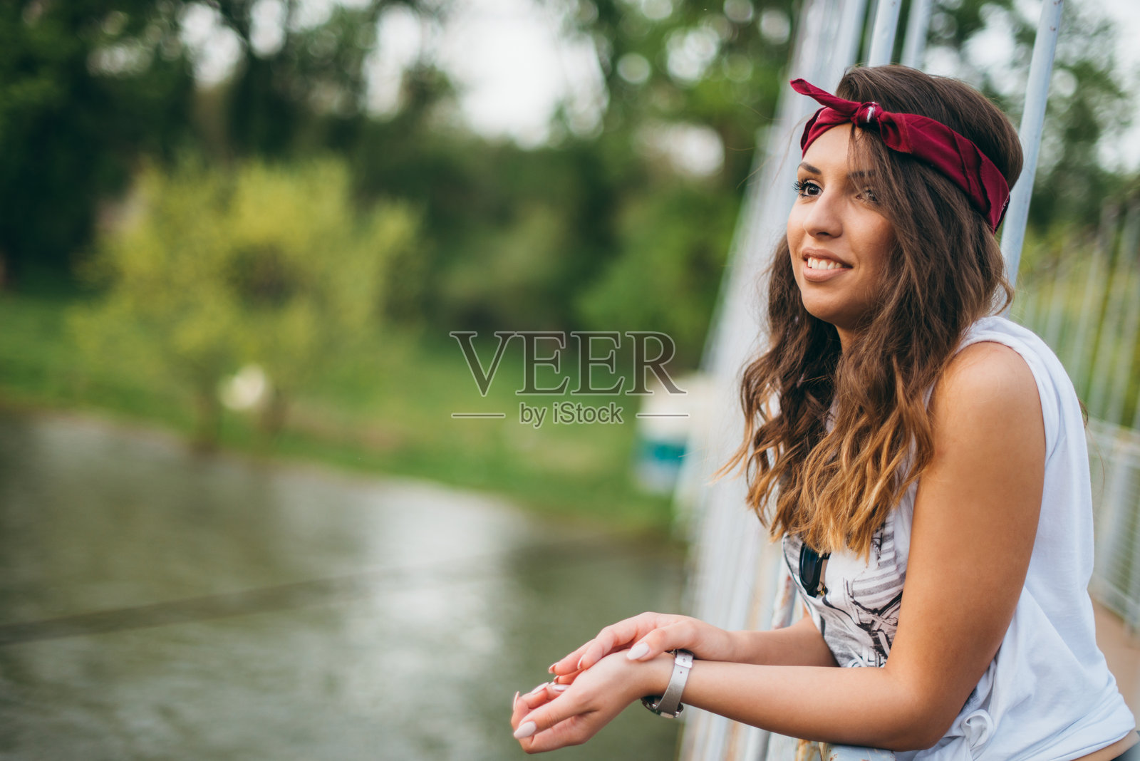 阳光明媚的日子里，穿着休闲服的女性微笑着，头戴红色头巾。照片摄影图片