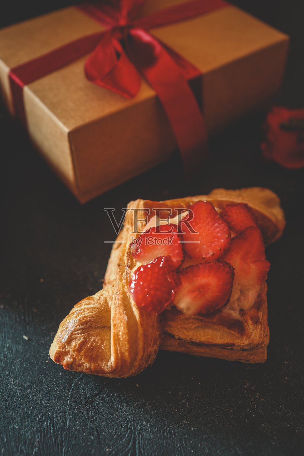 酥皮点心上放着新鲜草莓和奶油，置于深纹理表面上照片摄影图片