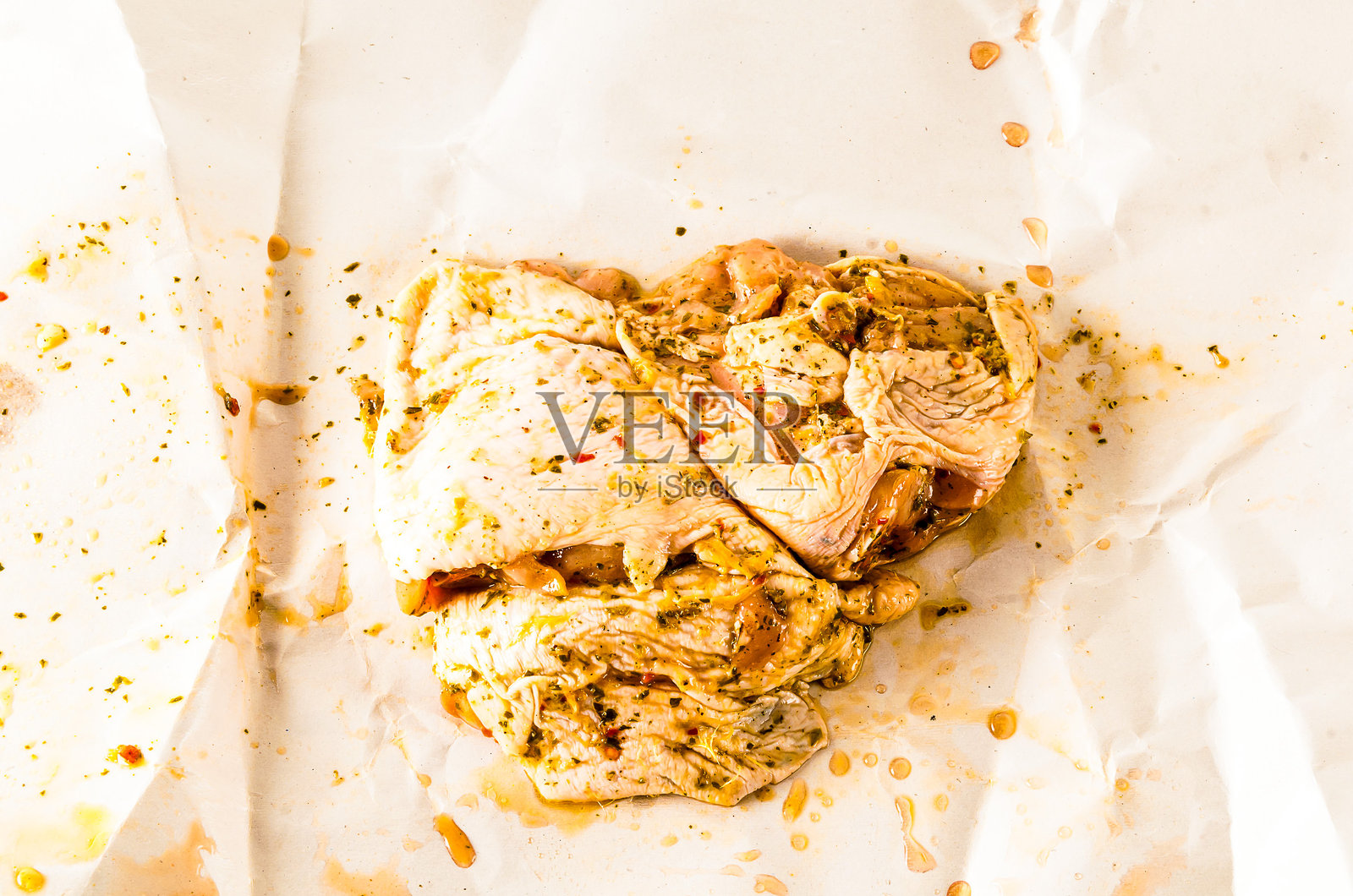 一块鸡肉上撒满香料，放在一张纸上。照片摄影图片