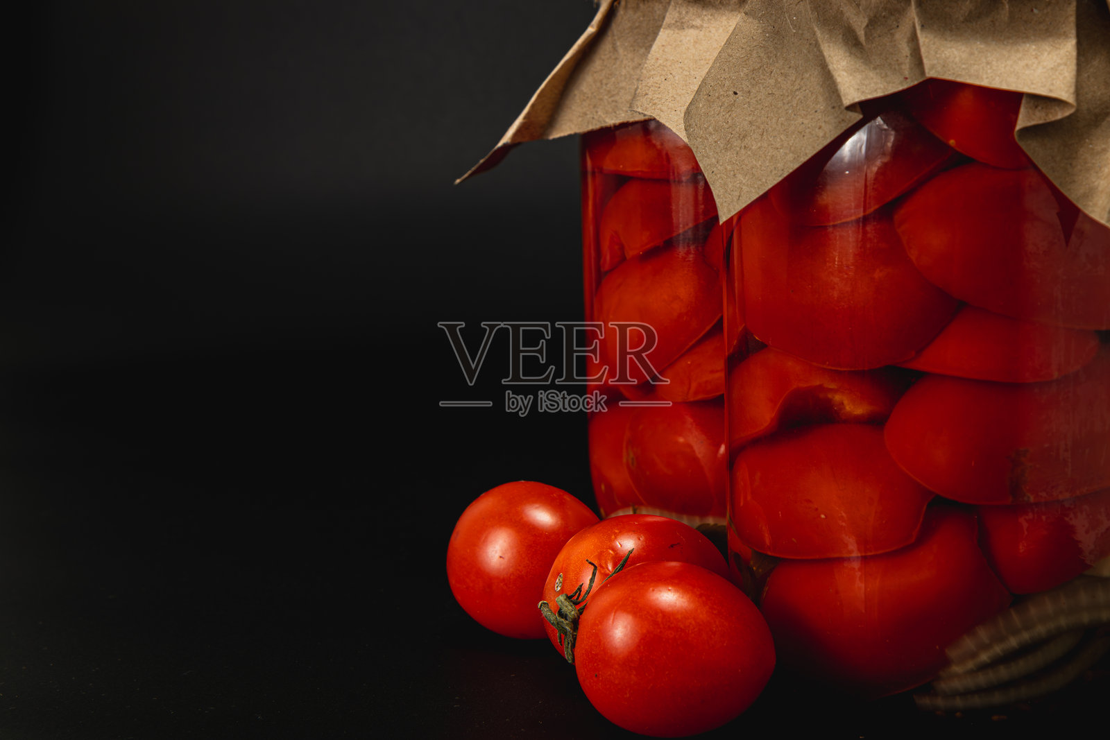 腌制番茄装在罐子里，旁边有新鲜番茄，放在深色表面上照片摄影图片