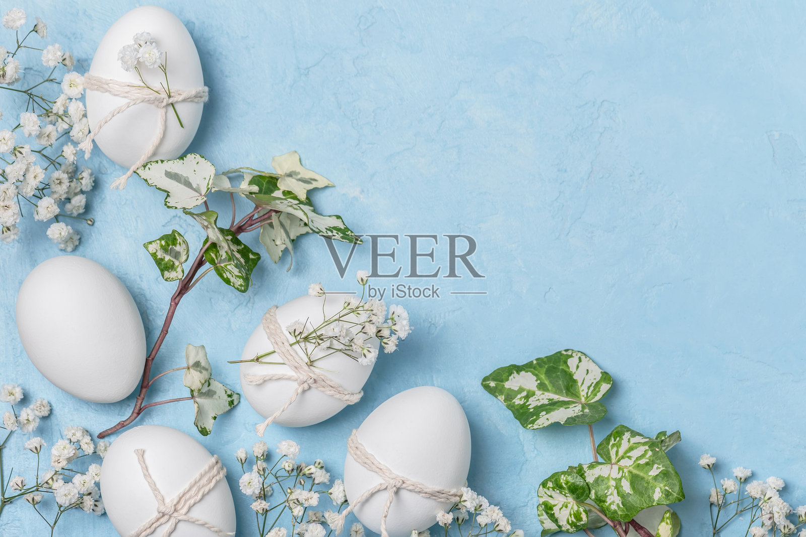 白色复活节彩蛋用麻绳和满天星装饰，背景为蓝色。复活节问候概念。复活节背景。照片摄影图片