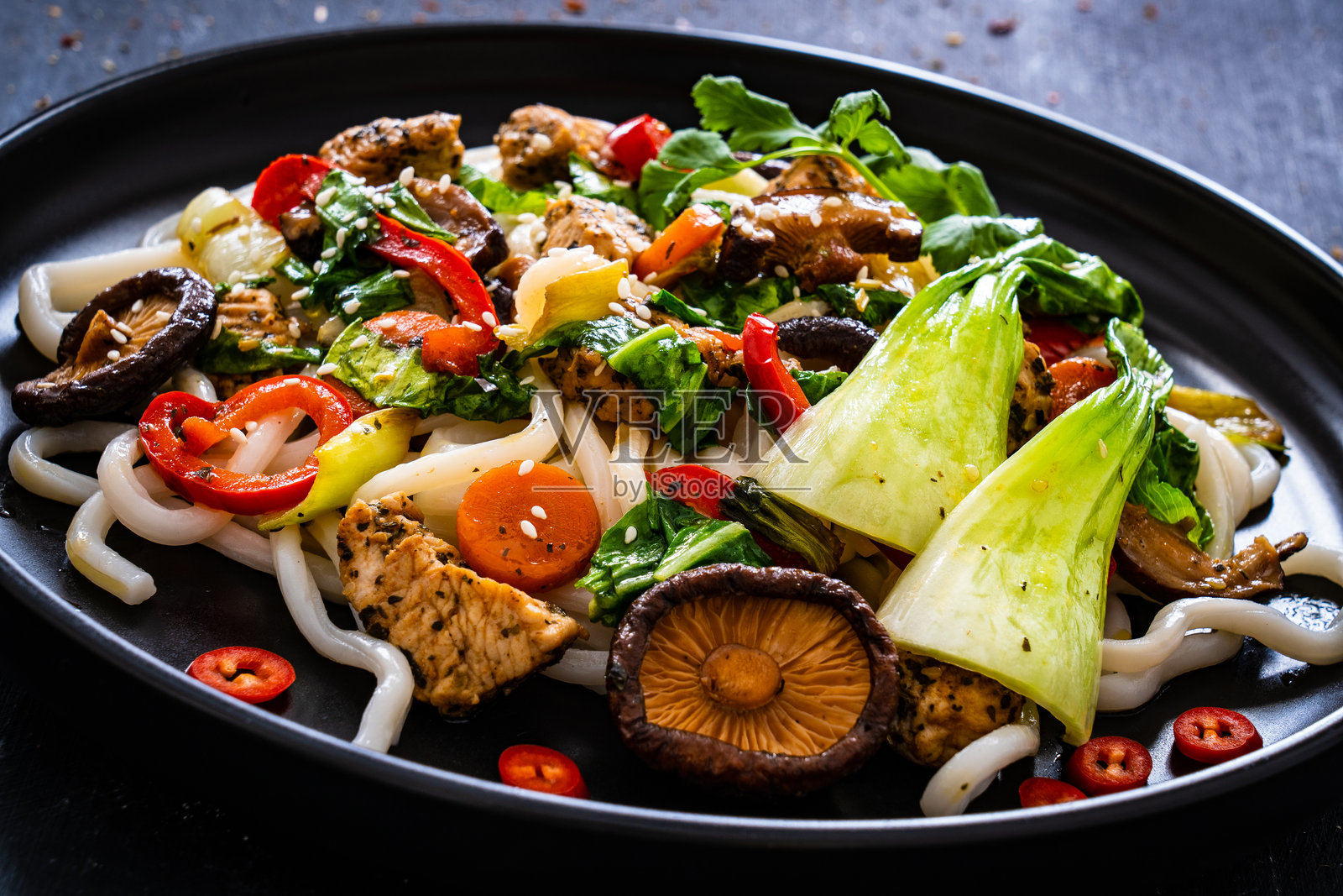 黑色桌子上的鸡块、面条和炒蔬菜照片摄影图片