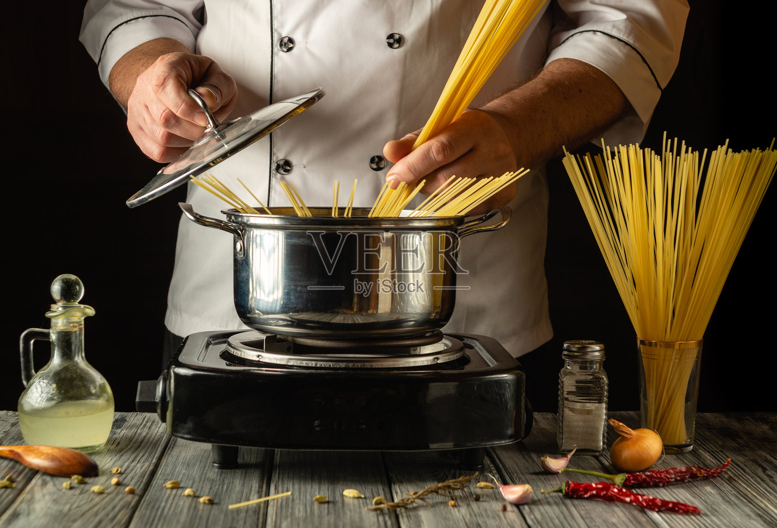 一位熟练的厨师准备烹饪意大利面，将新鲜的面条放入闪亮的锅中。厨房台面上摆满了食材，展现了对烹饪艺术的热爱。照片摄影图片