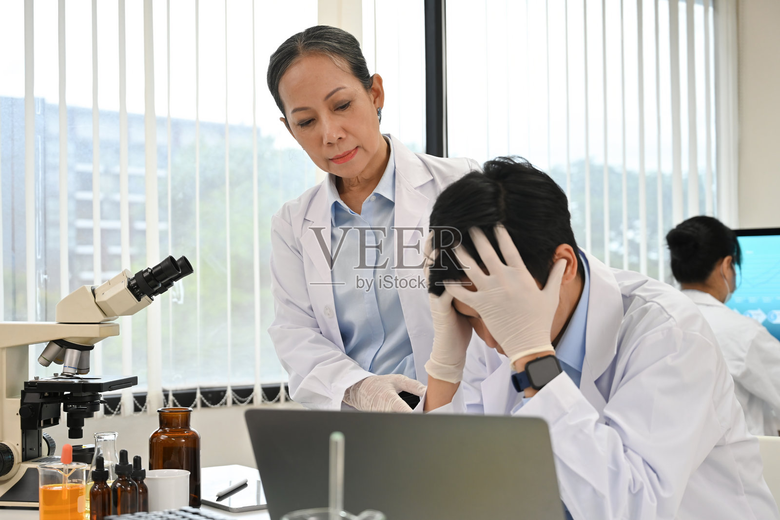 一位年长的女性科学家安慰一位因研究项目失败或工作压力而感到沮丧的男性同事照片摄影图片