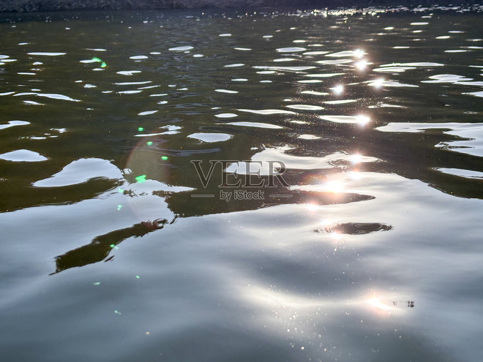 水面平静而宁静，泛起涟漪，映照着阳光的倒影。照片摄影图片