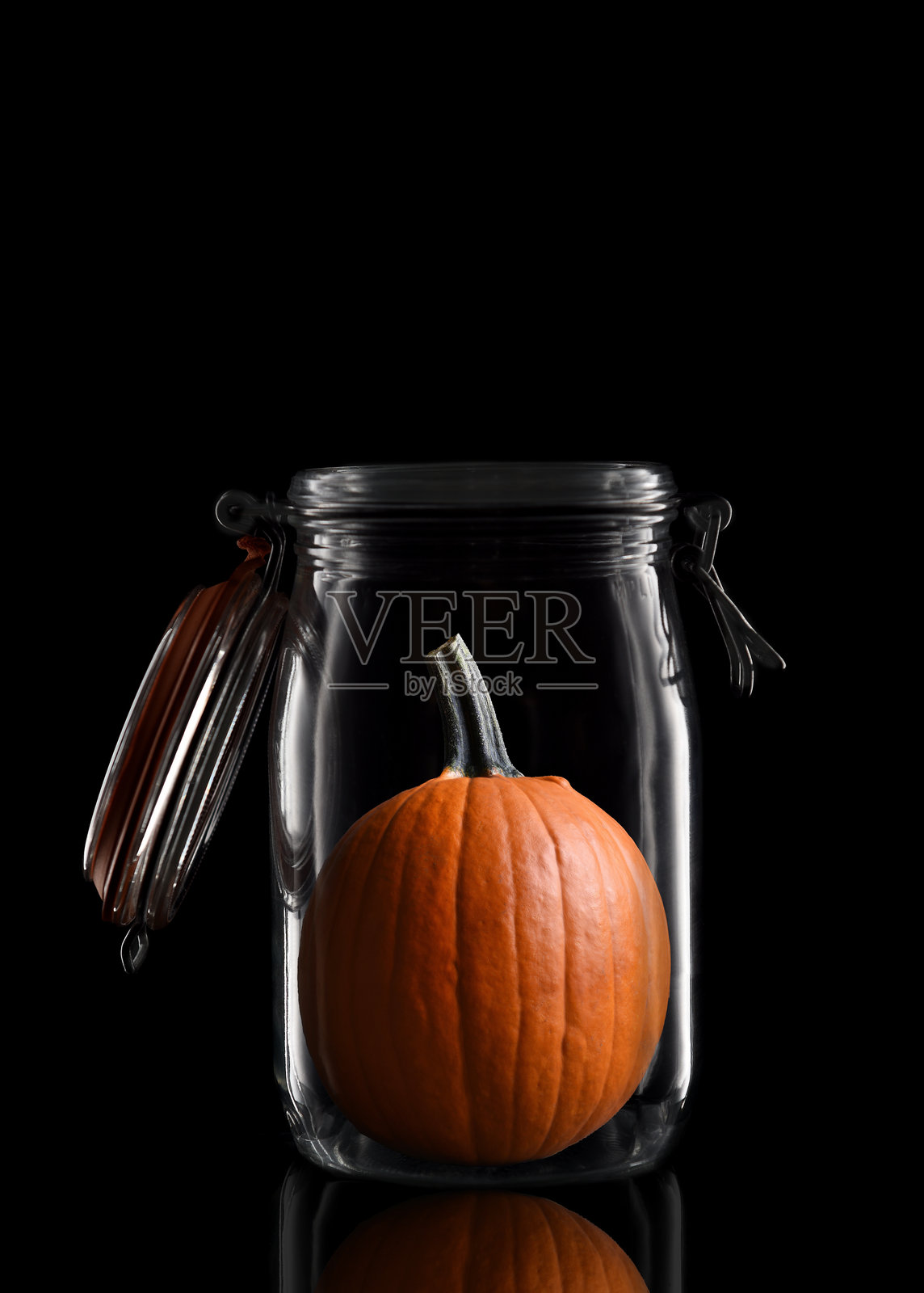 一个装在玻璃储存罐或罐头瓶中的南瓜，孤立在黑色背景上，带有反射，盖子打开。照片摄影图片