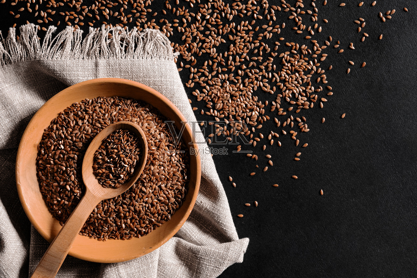 健康谷物。桌子上散落着一勺亚麻籽和一个木盘。照片摄影图片
