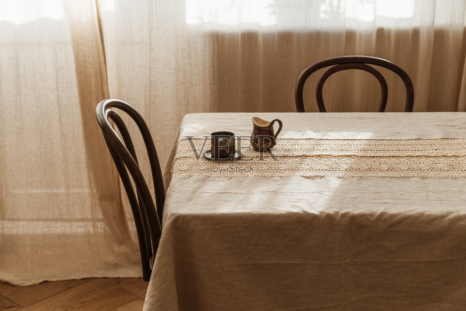 一个优雅的单人早餐，桌上摆放着茶或咖啡的杯子和一个牛奶壶，桌子上铺着带蕾丝的亚麻桌布，阳光明媚的夏日，乡村别墅中。照片摄影图片