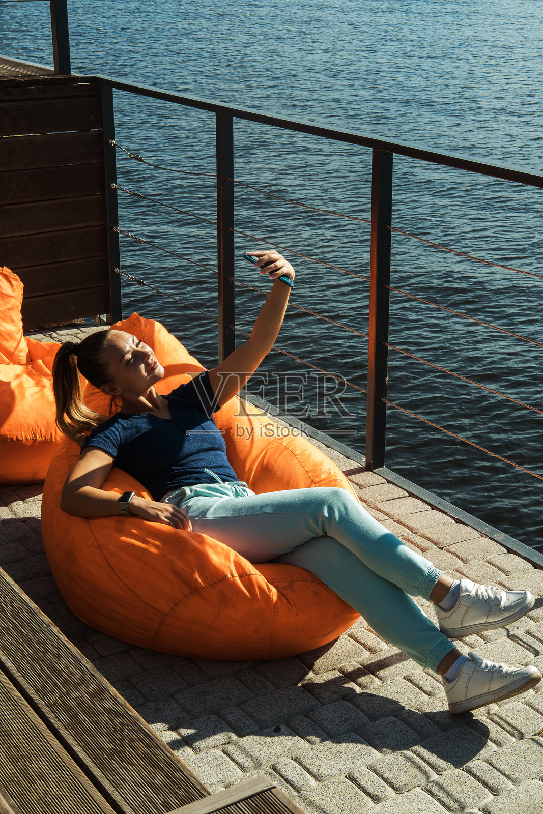 女人坐在充气豆袋椅上，在河边的沙滩上放松。照片摄影图片