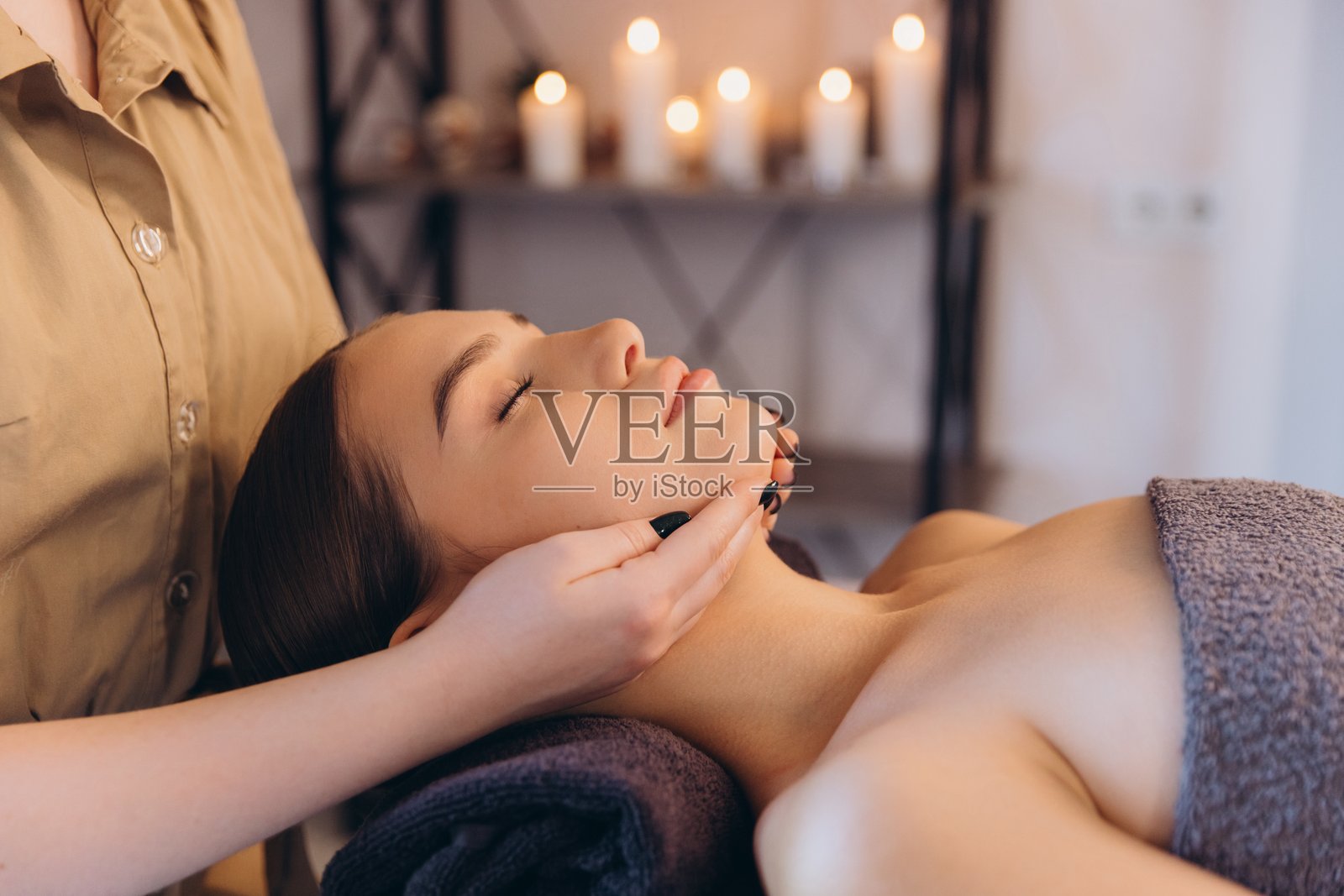 按摩治疗师正在为年轻女性进行放松的面部按摩照片摄影图片