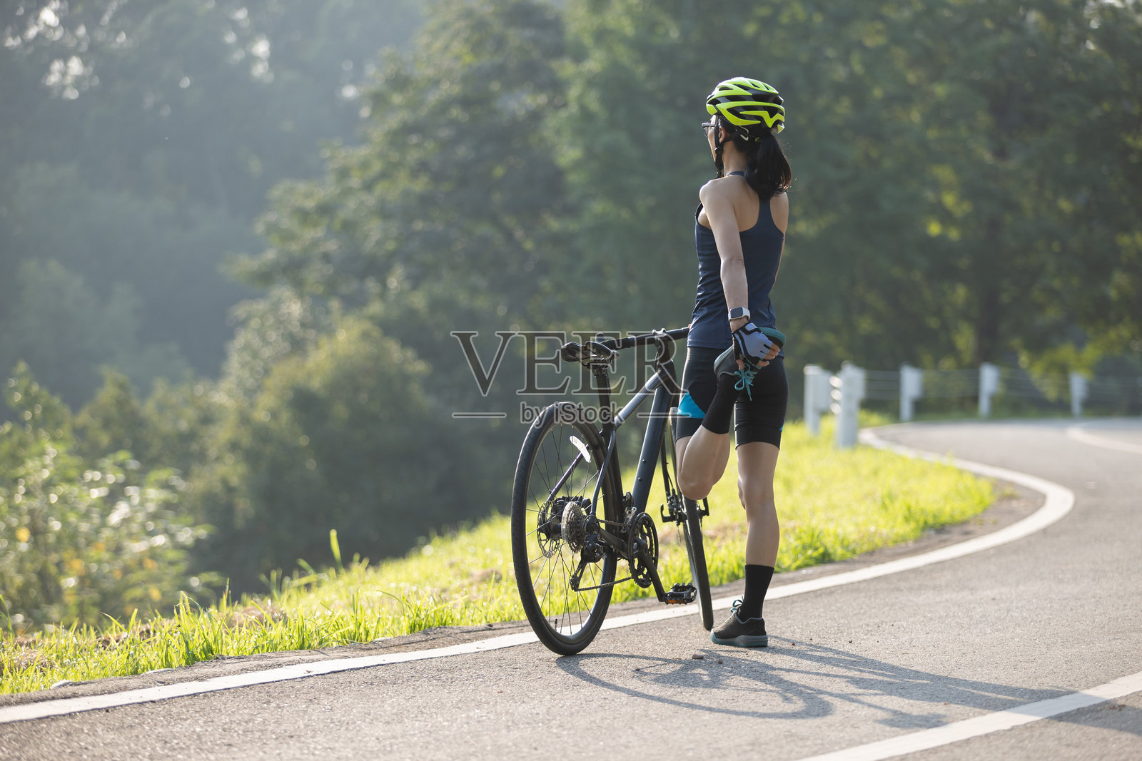 夏季公园小径上伸展腿部的女性骑自行车者照片摄影图片