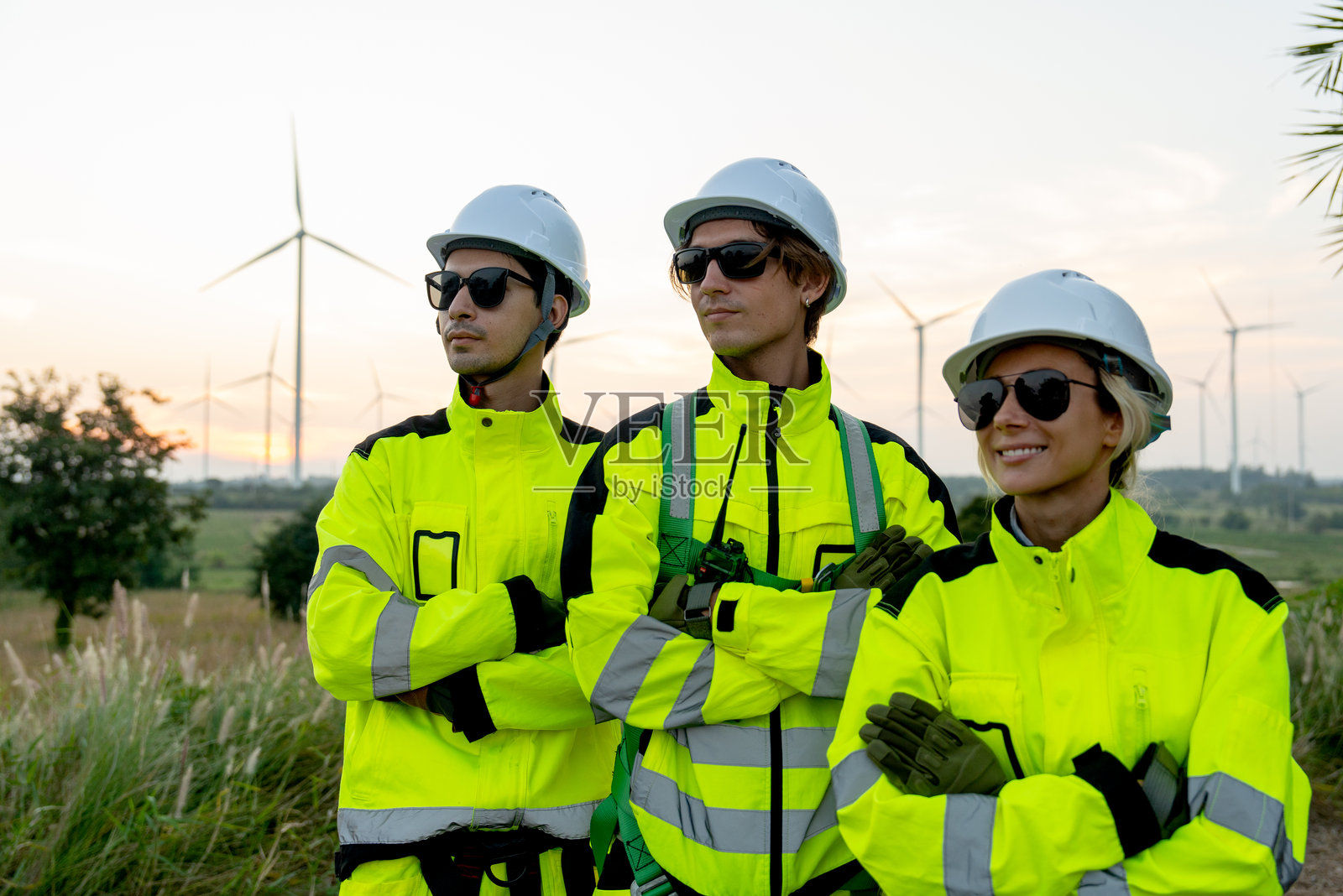 一组风力发电机工作人员或技术人员的肖像，他们双臂交叉，向右侧看，背景是一排风力发电机。照片摄影图片