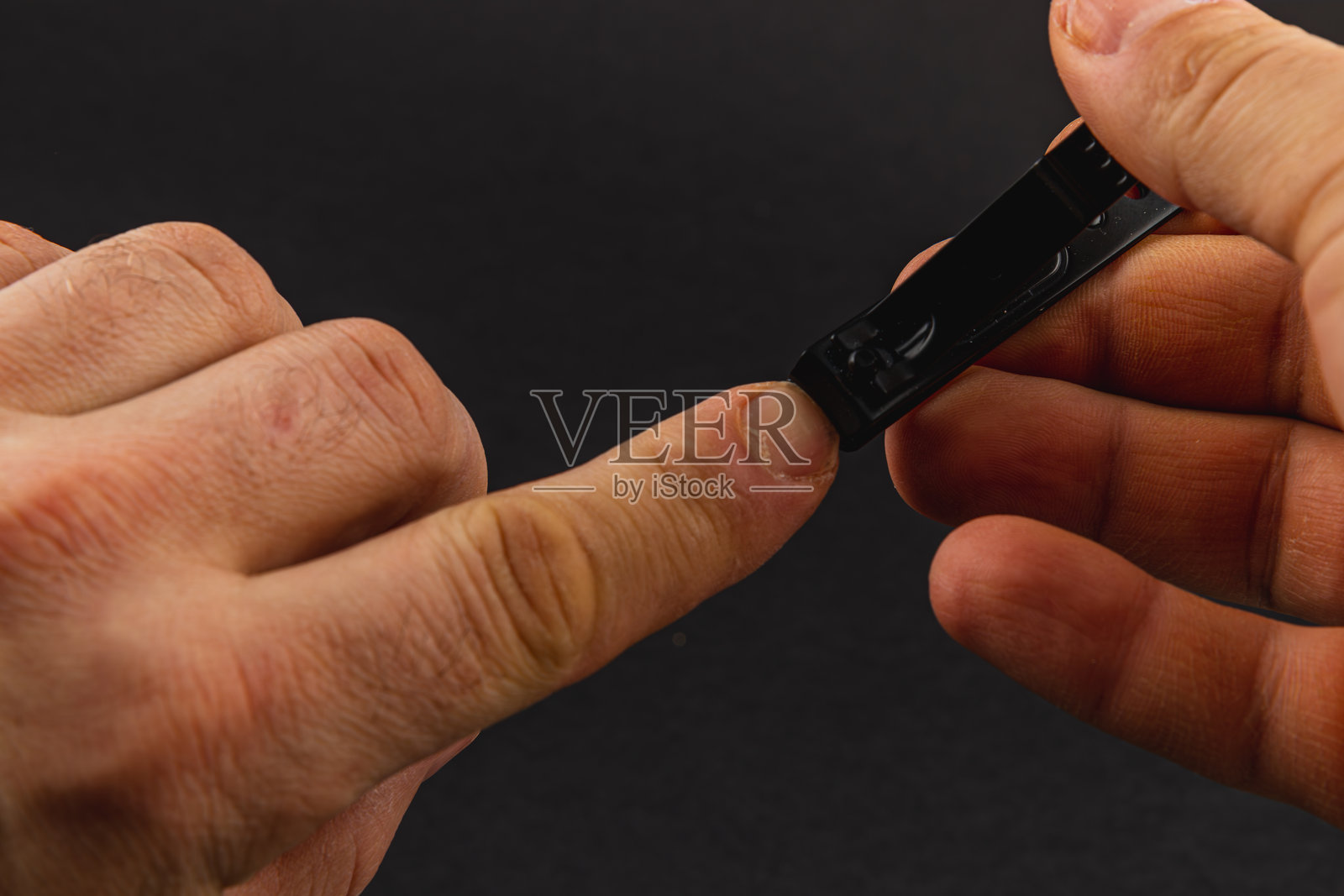 男性手部在黑色背景下使用指甲剪修剪指甲照片摄影图片