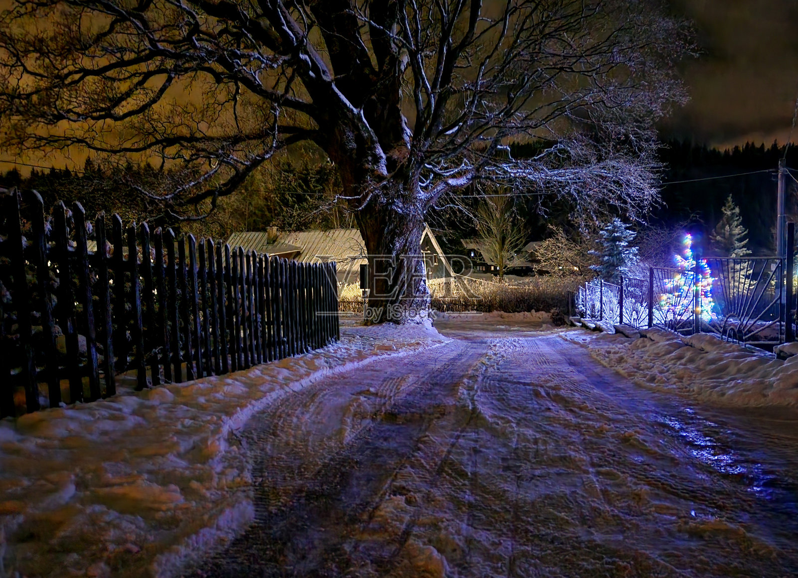 圣诞氛围，雪-covered的道路和古老的树木。然而，有人用冰链装饰了一棵小云杉。街边的灯旁有一堆雪。照片摄影图片