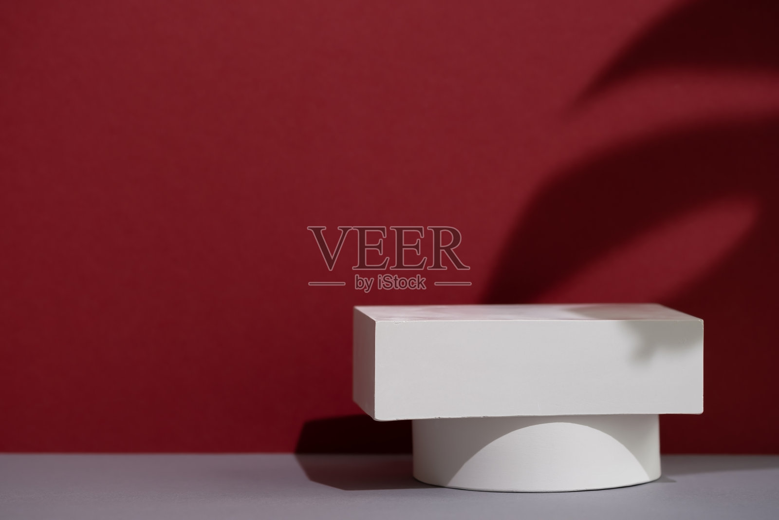 几何白色场景，灰色和酒红色背景上有一片龟背竹叶的阴影。一个用于广告和产品展示的高档展台。展示柜。照片摄影图片