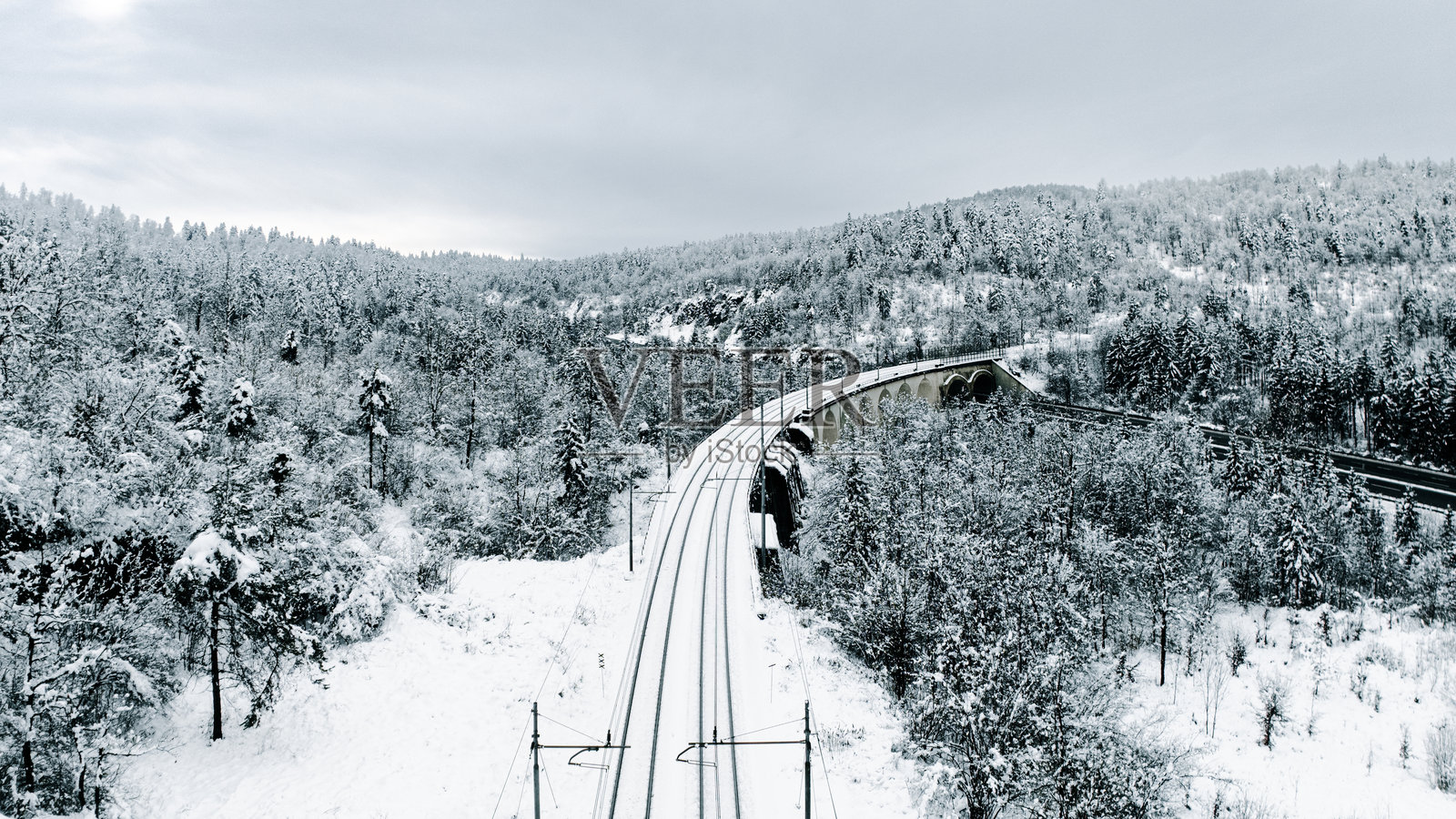 冬季铁路穿过被雪覆盖的森林和山丘照片摄影图片