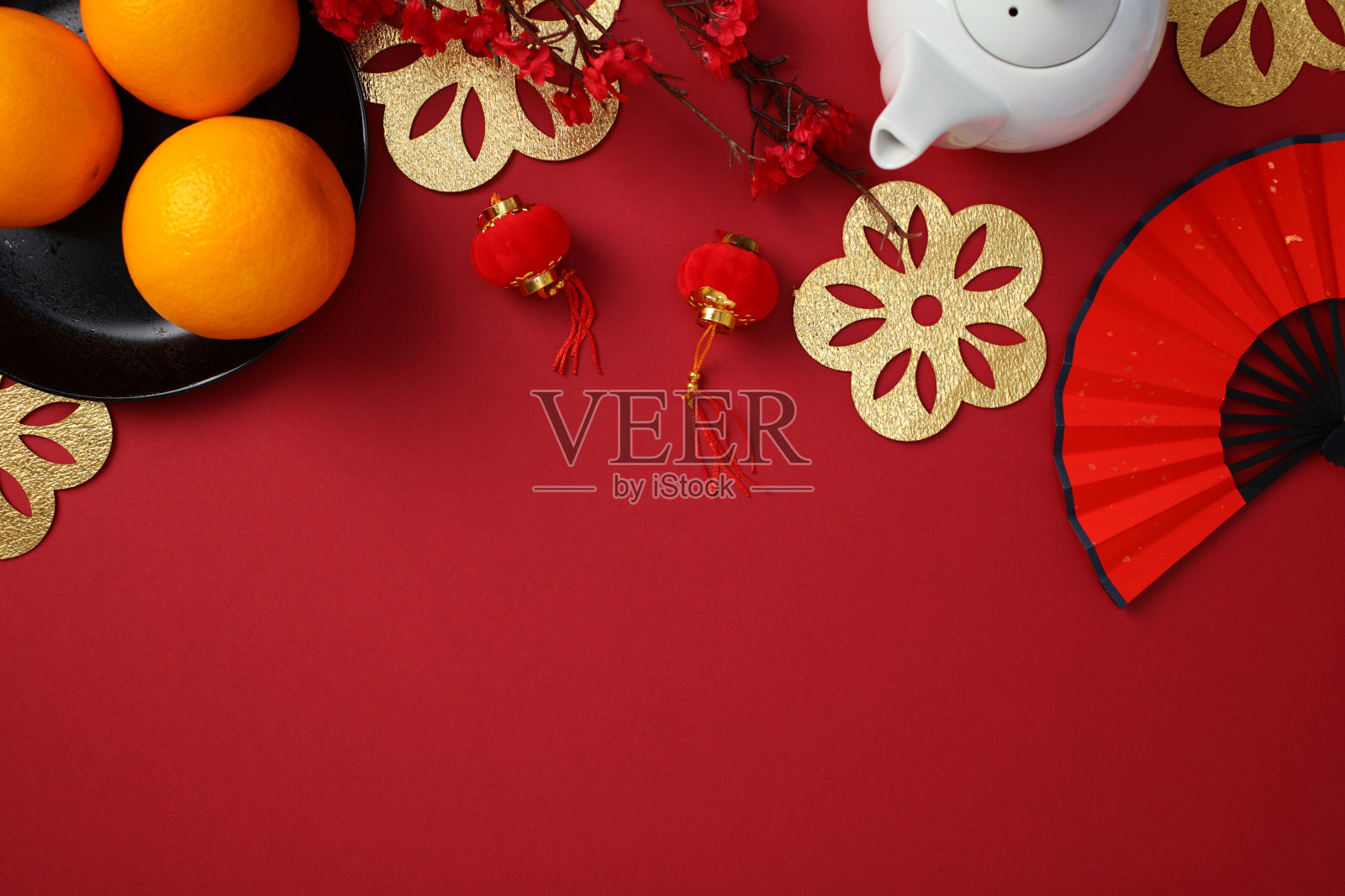 春节扁平布局，包含橙子、红色扇子、茶壶、金色装饰和红灯笼，背景为红色。照片摄影图片