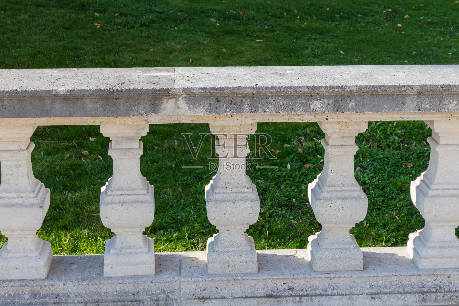 阳光照射下的石栏杆部分，映衬在阴影中的草坪上照片摄影图片