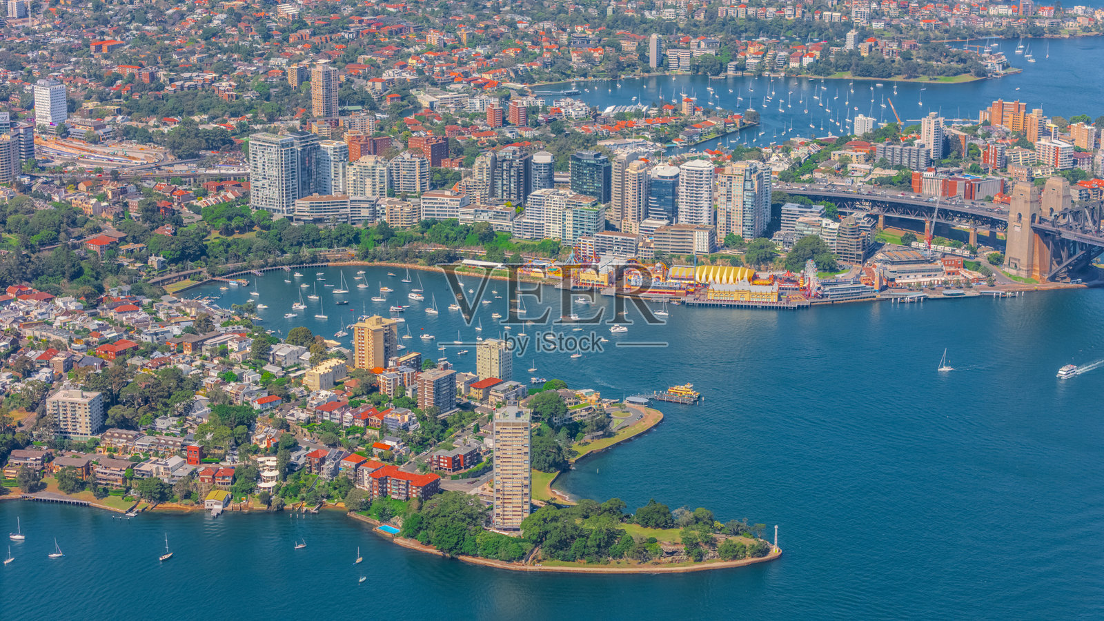 悉尼港的鸟瞰图，包含巴尔曼、达令港、悉尼中央商务区、贝壳湾码头、北悉尼、悉尼海港大桥、薰衣草湾、米尔森角和曼利，展现了一个温暖的夏日蓝天。照片摄影图片