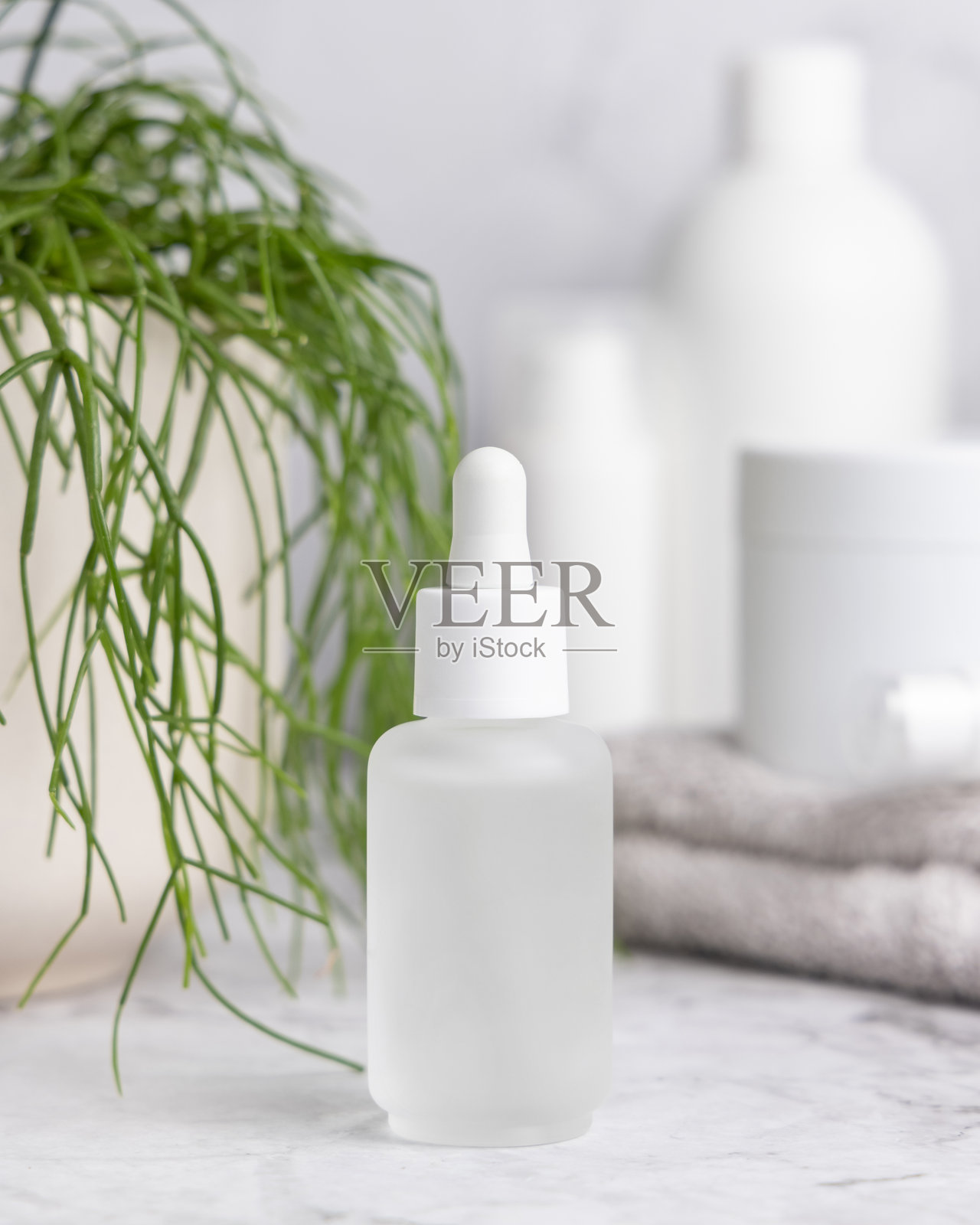 白色玻璃滴管瓶靠近绿色植物的近景，化妆品样机照片摄影图片
