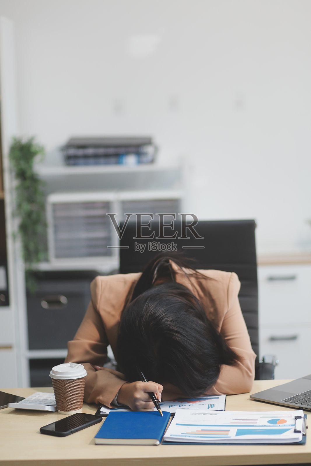 疲惫的年轻亚洲女商人在办公室处理税务文件和笔记本电脑。忧伤、不快乐、担忧、抑郁或员工生活压力的概念。照片摄影图片