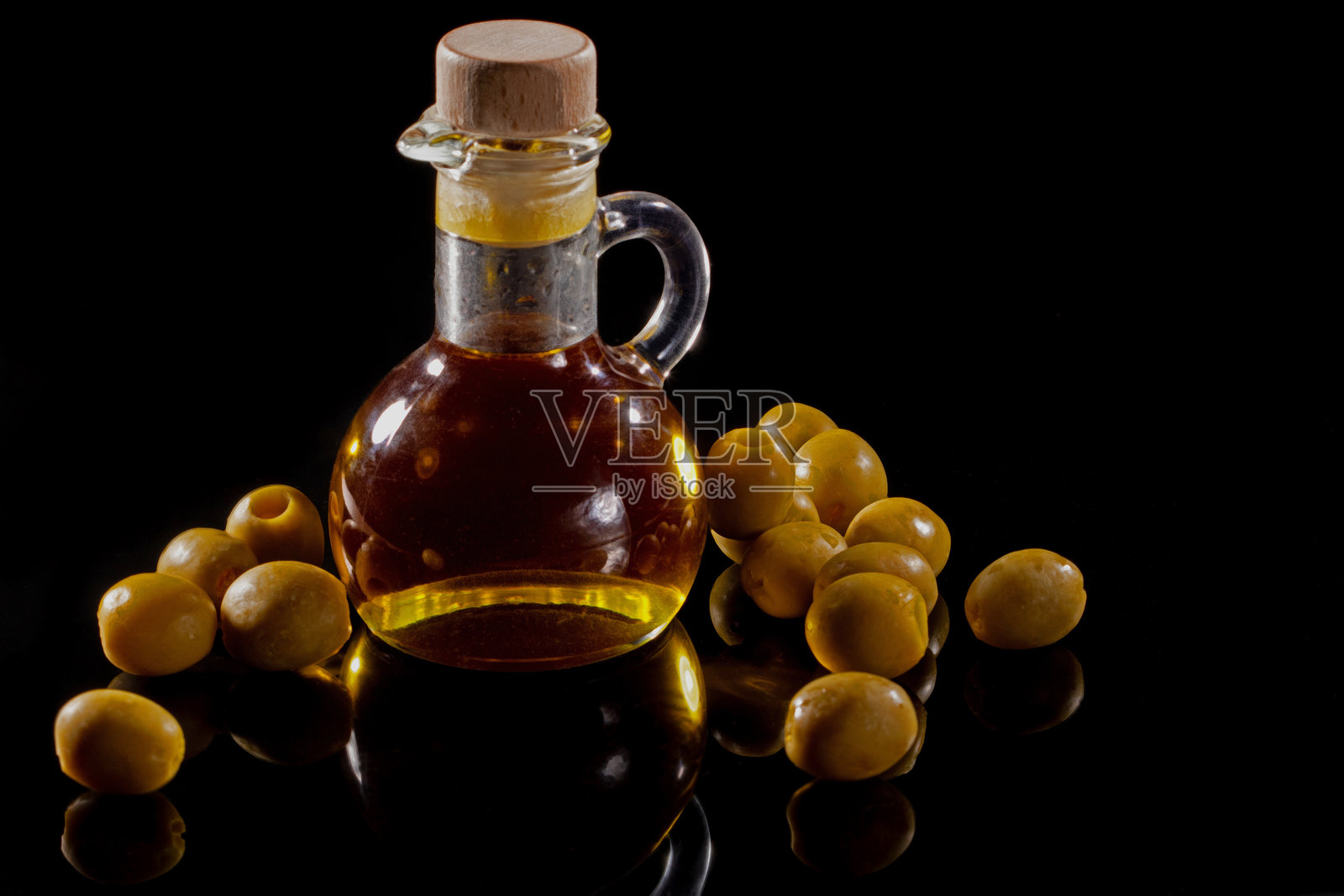 黑色镜面背景上的橄榄油玻璃壶和散落的橄榄照片摄影图片