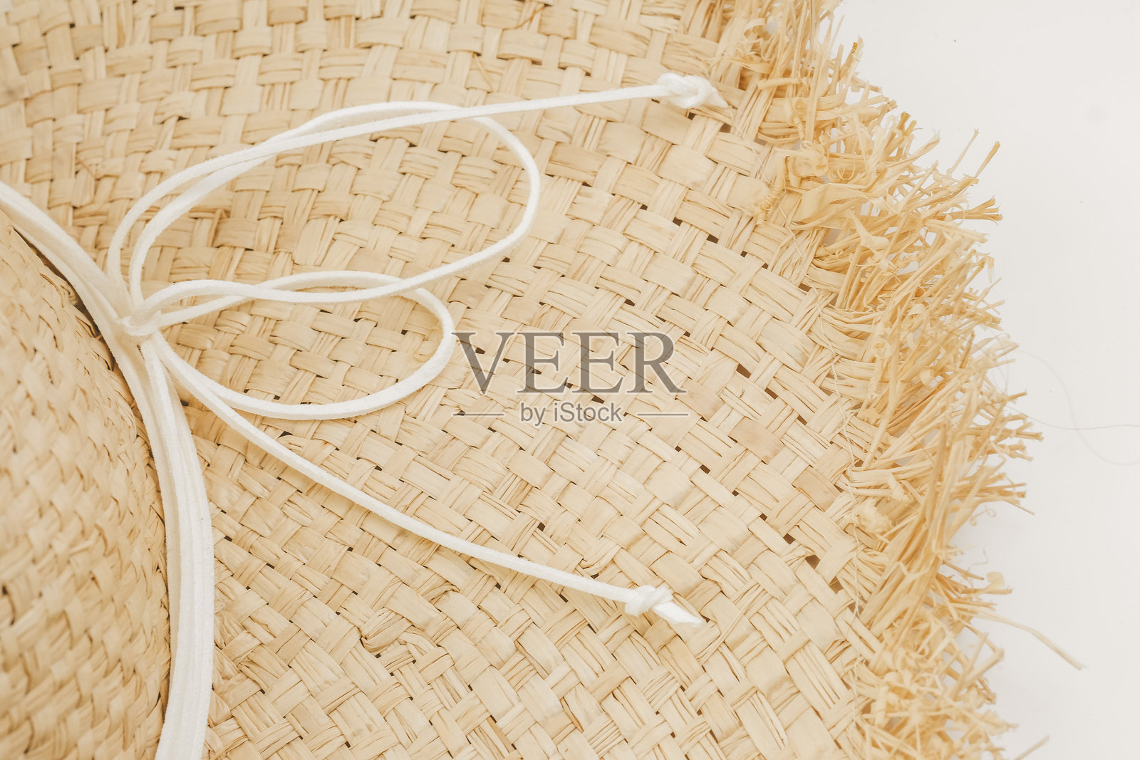 一顶特写的编织草帽，周围系着一根白色绳子，边缘有流苏。照片摄影图片