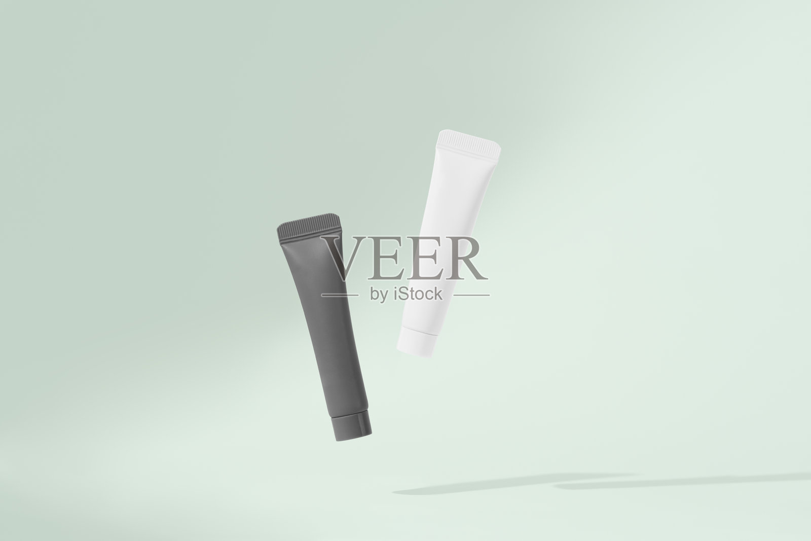 白色和黑色的管子在绿色背景上悬浮，带有投影。这是面部肌肤自然护理化妆品的概念，展示美容产品。照片摄影图片