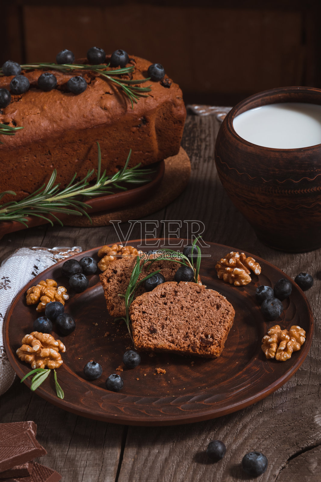 巧克力杯子蛋糕切成块，放在木桌上的陶土盘子里，配有牛奶和蓝莓照片摄影图片