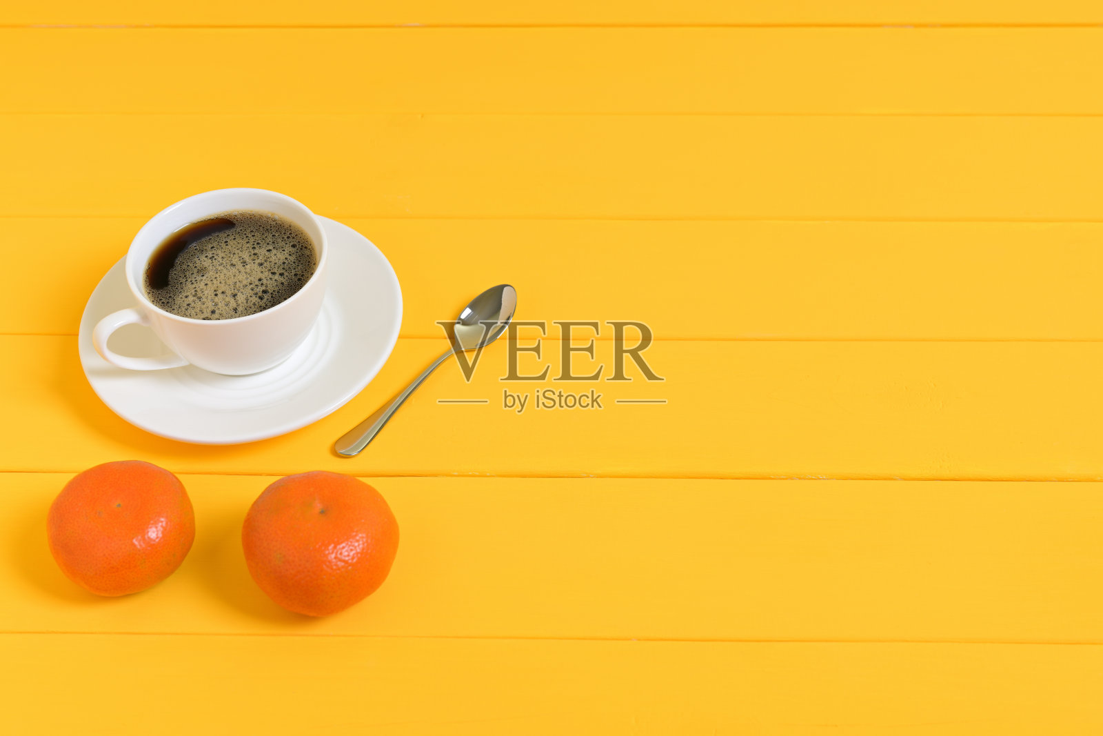 黄色背景上的咖啡杯、勺子和两个橘子照片摄影图片