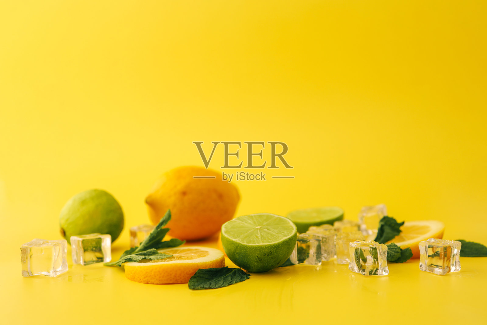 新鲜的柠檬、青柠、薄荷叶和冰块排列在鲜艳的黄色背景上。这是一幅清新多彩的构图，完美适合夏季主题和饮品展示。照片摄影图片