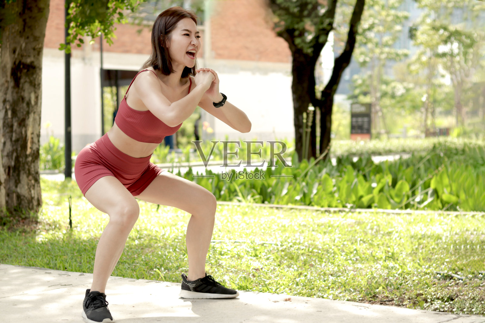 短发运动女孩穿着运动服在户外公园做深蹲锻炼。快乐微笑的亚洲女性在户外绿花园进行健身和身体训练。照片摄影图片