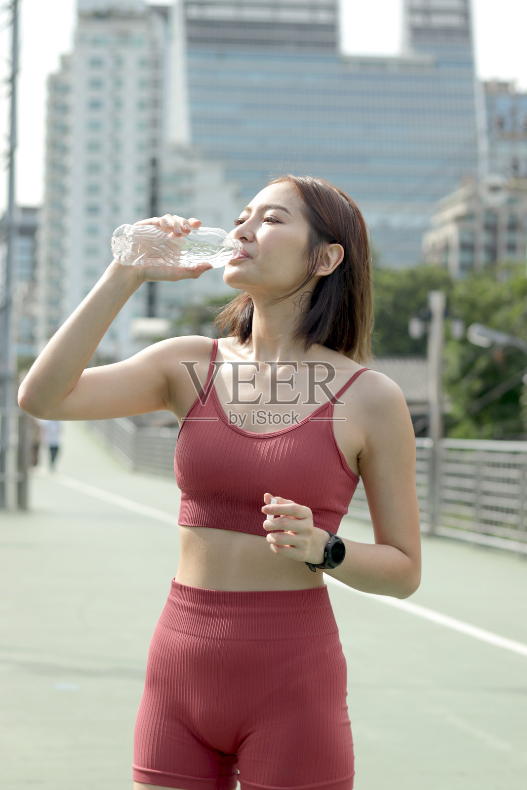 短发运动女孩穿着运动服，手持水瓶，在城市街道上慢跑锻炼后休息。快乐微笑的亚洲女性喝水以提神。照片摄影图片