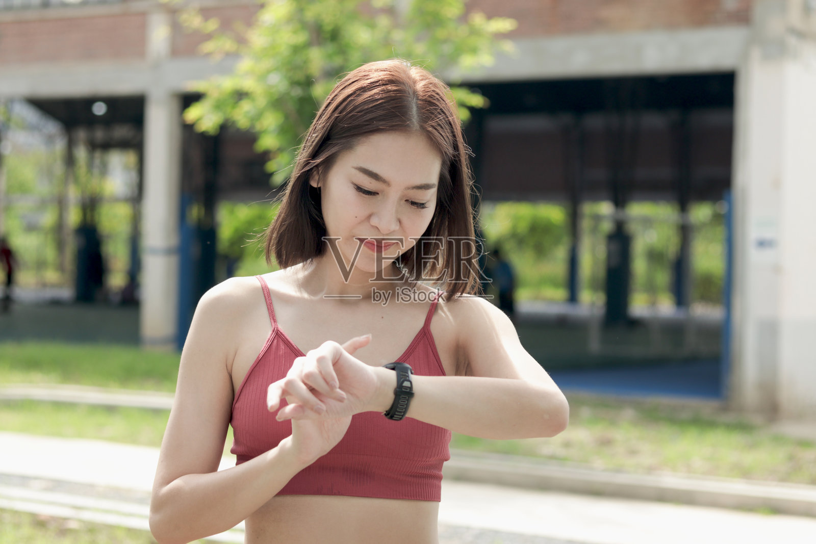 短发运动女孩穿着运动服，在户外公园慢跑后查看和触摸智能手表。快乐微笑的亚洲女性在绿色花园中进行健身运动。照片摄影图片