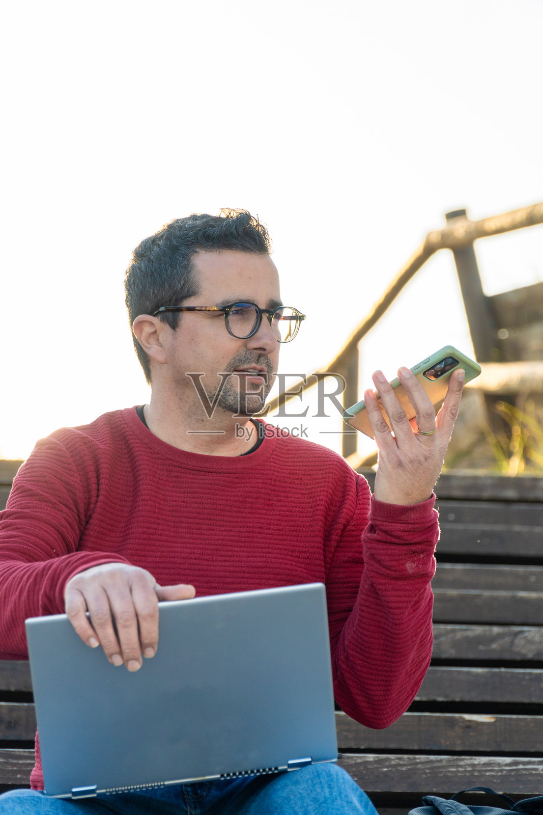 一名数字游牧者在笔记本电脑上工作，同时用手机录音。照片摄影图片