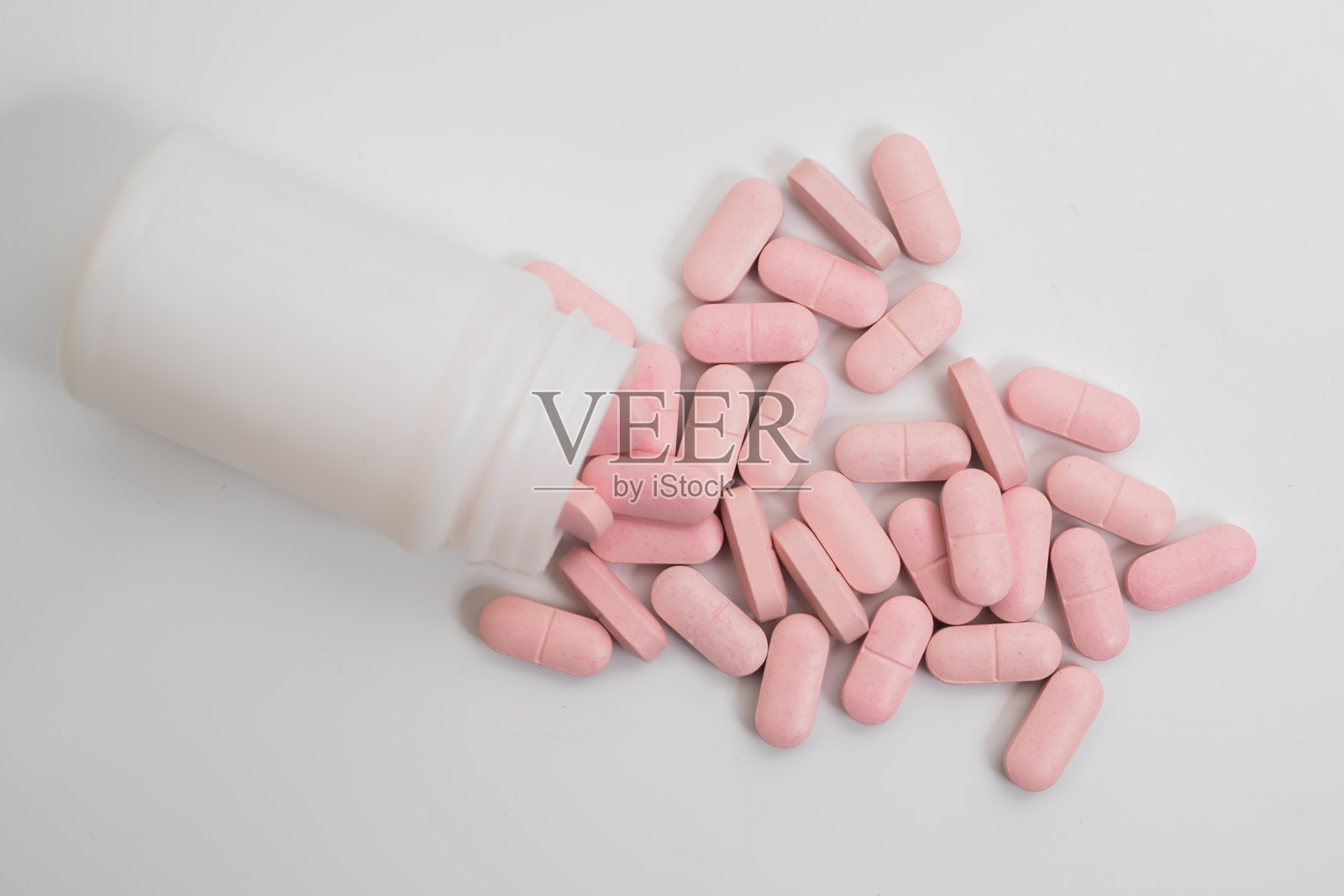 粉色药丸从白色药瓶中洒落在干净的白色背景上照片摄影图片