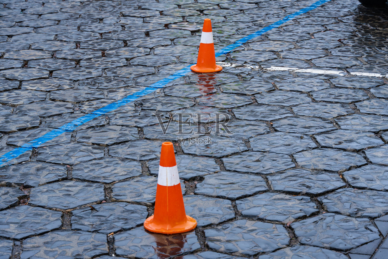 交通锥被放置在湿滑的鹅卵石街道上，标记着城市区域内的施工区域，正值下雨时。照片摄影图片