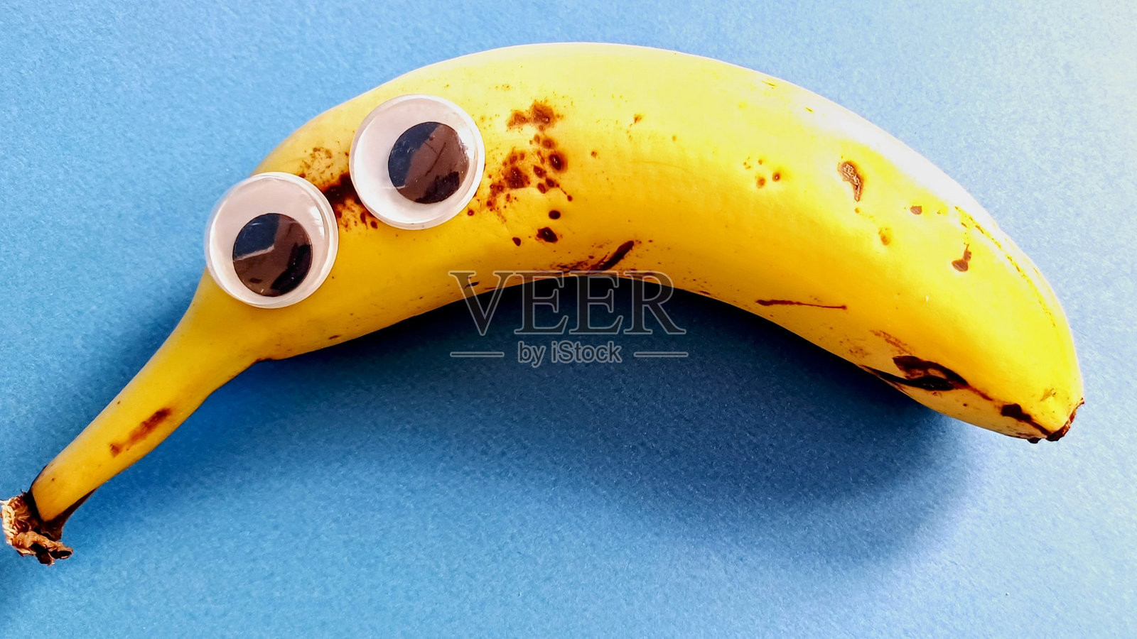 蓝色背景上的香蕉和香蕉上的塑料玩具眼睛。搞笑的表情照片摄影图片