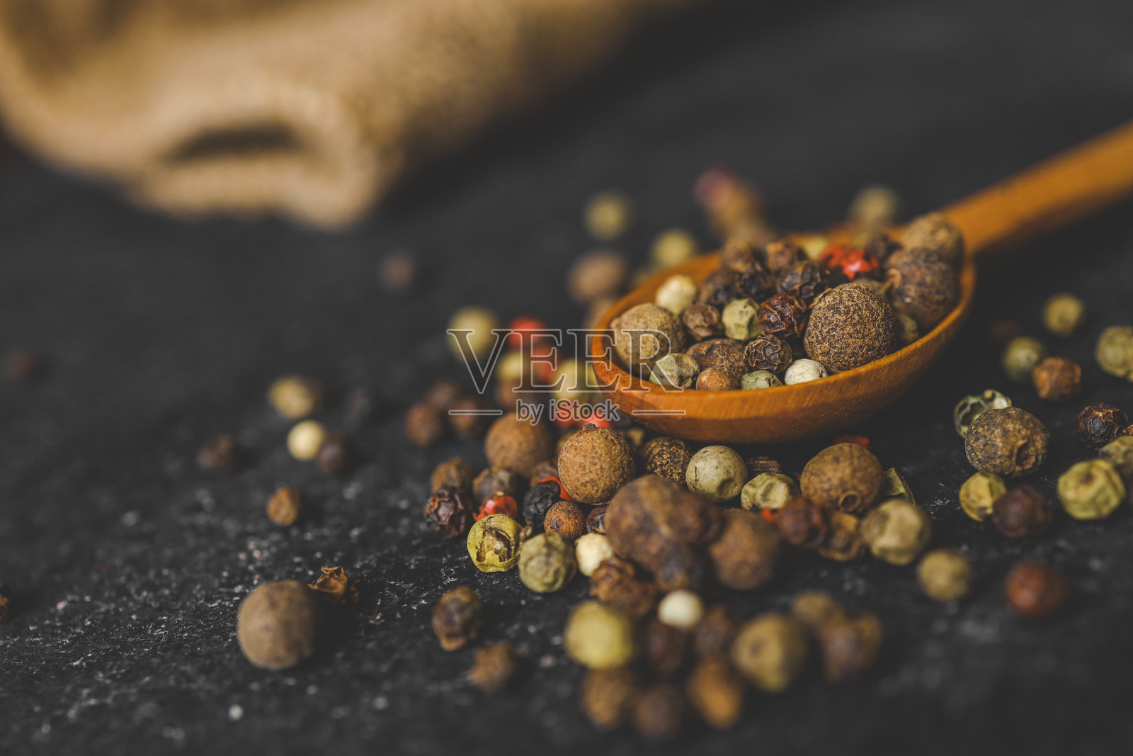 从上方看一只装满五彩胡椒粒的木勺，散落在深色纹理表面上。非常适合烹饪、香料和食材主题的概念。照片摄影图片