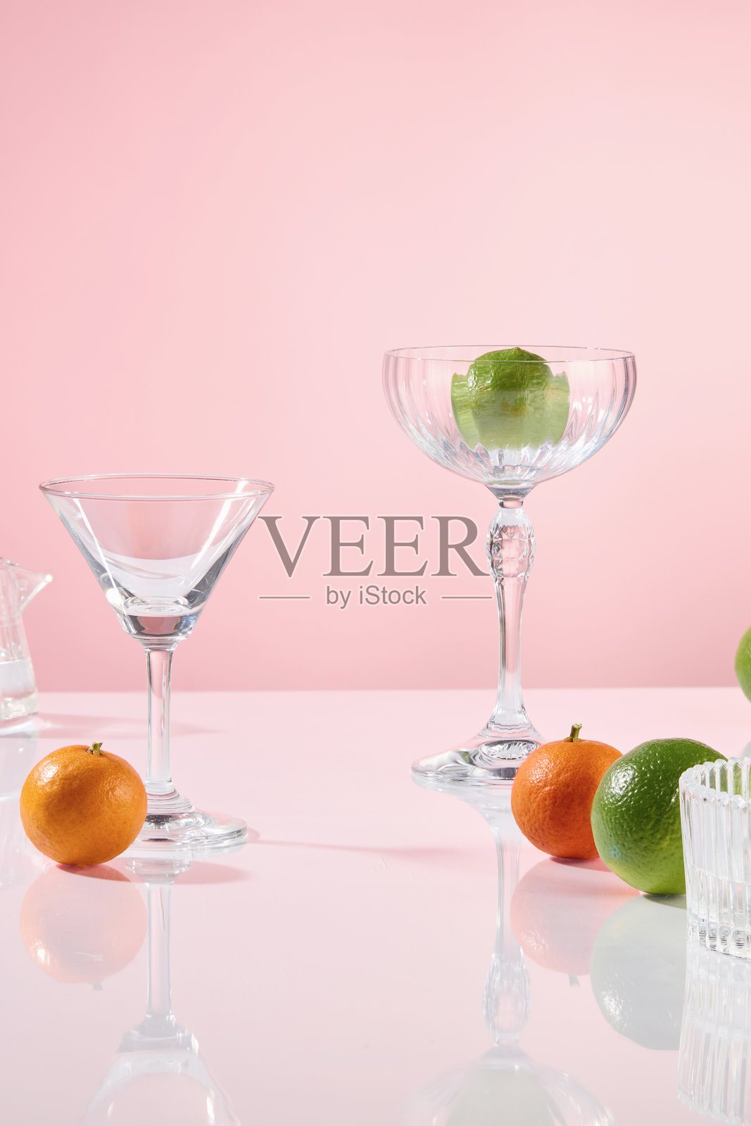 派对概念的化妆品广告照片，背景为粉色。旁边有鸡尾酒杯，装饰着一些柠檬水果，放置在玻璃表面上，留有空位以摆放产品。照片摄影图片